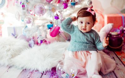 Pretty little child sits on fluffy carpet before Christmas tree